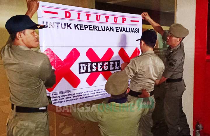 Petugas Satpol PP Blitar memasang plakat "Disegel" pada salah satu karaoke yang ditutup di Blitar. foto: AKINA/ BANGSAONLINE