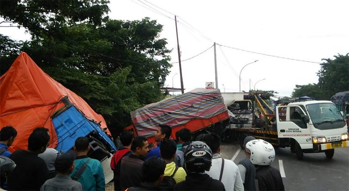 Mobil derek berupaya mengangkat truk gandeng yang masuk ke dalam parit.