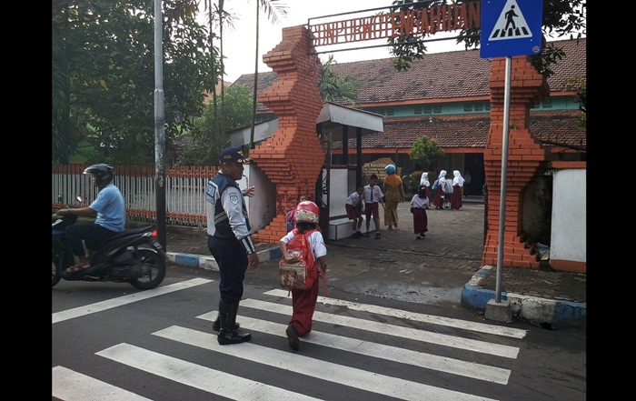 Petugas Dishub saat menyebrangkan anak sekolah.