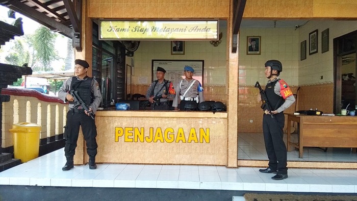 Petugas kepolisian berpakaian lengkap dengan rompi anti peluru, helm, dan senjata laras panjang siaga di depan gerbang markas Polres Blitar Kota.