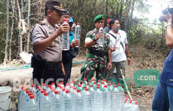 Petugas menunjukkan arak siap edar yang diproduksi di tengah hutan Desa Ngino. foto: GUNAWAN WIHANDONO/ BANGSAONLINE